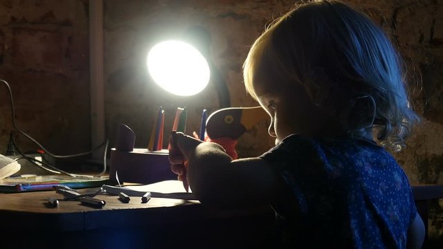Kid is drawing in the album. Little girl, child sits near the window and painting