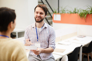 Young casual manager talking to his colleague in office while pointing at paper during working meeting