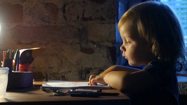 Kid is drawing in the album. Little girl, child sits near the window and painting