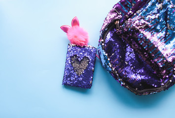Bright composition of fashion accessories. Glitter sequins backpack, notepad, funny pen, nail polish. Different objects on soft pastel background. Flat lay, top view