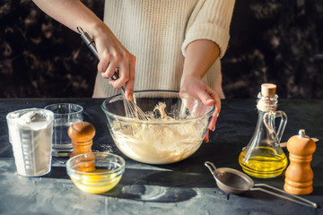 Beautiful female hands knead the dough from which they will then make bread, pasta or pizza. The background is dark