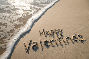 Happy Valentine's Day message handwritten in smooth sand copy space with foamy wave 