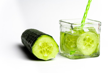 square glass with a straw to drink filled with water with slices of fresh cucumber