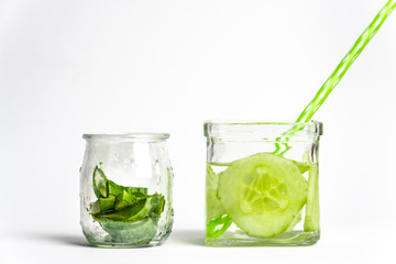 square glass with a straw to drink filled with water with slices of fresh cucumber