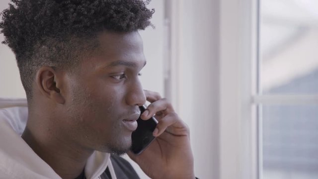 Close-up of smiling young man talking on mobile phone indoors. Face of African American male student having conversation on smartphone. Communication technology concept