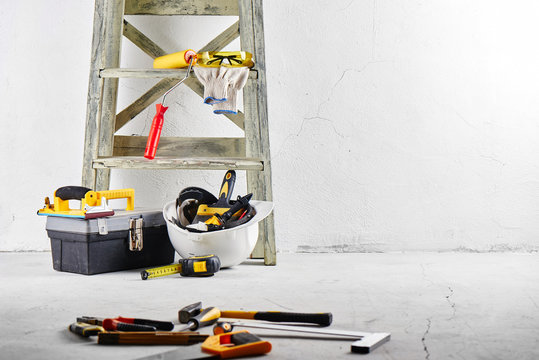 Construction tools and stepladder on a white wall background. Repairs