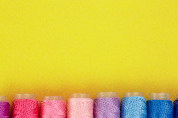 Colorful thread spools over bright yellow background, above view