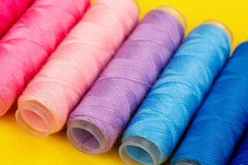 Group of colorful spools of thread used to sewing, needlework and embroidery over bright yellow background