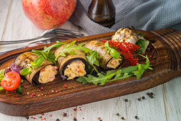 Eggplant rolls on a wooden board with a pomegranate and a fork in the background