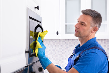 Male Janitor Cleaning Oven With Napkin