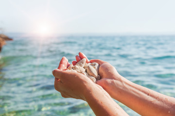 Female hands on the background of sea or ocean are holding sea stones.