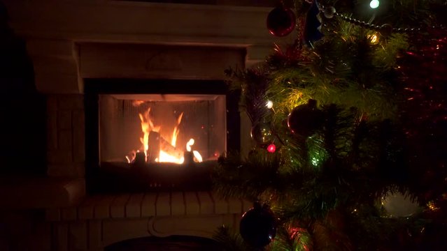 Amazing Christmas tree blinking colorful lights garland near fireplace with burning fire log. Beautiful cosiness holiday home interior enjoying winter vacation atmosphere