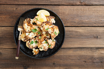 Black plate with tasty grilled cauliflower on wooden table.