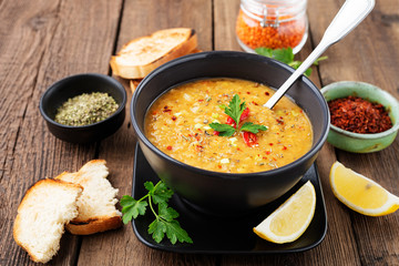 Lentil soup with  bread in a dark ceramic  bowl on a wooden background .