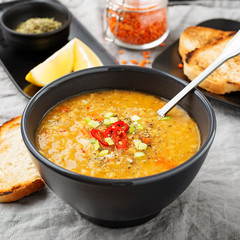 Lentil soup with  bread in a dark ceramic  bowl on a gray textile background .