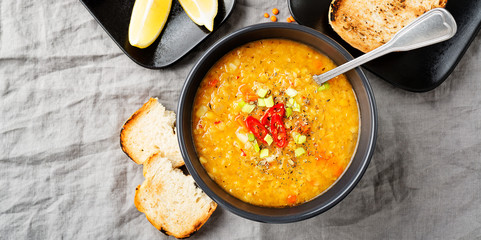 Lentil soup with  bread in a dark ceramic  bowl on a gray textile background .