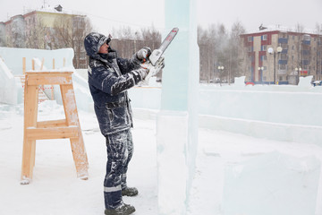 The sculptor cuts a figure from an ice block with a gasoline saw