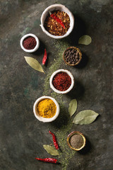 Spices seasoning and herbs variety in ceramic bowls. Different ground peppers, chili pepper, turmeric, bay leaf, cinnamon over dark metal background. Flat lay, space. Cooking concept