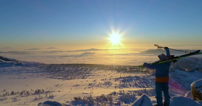 aerial view: skier on the mountain peak, skiing on his shoulder and big win position. sunrise, sunset. mountain valley. above the clouds. stock video footage. back light. camera goes linearly forward