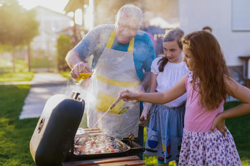 Proud cheerful grandfather teaching his grandchildren how to make a barbeque. Having fun in backyard on summer day.