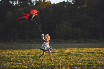 Cute little girl with long hair running with kite in the field on summer sunny day