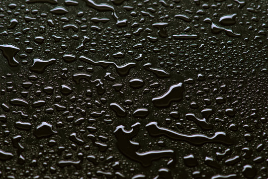 Glossy water droplets on black surface made of synthetic material
