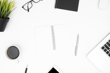 Blank notebook is on top of white office desk table with laptop, coffee cup and office supplies. Top view with copy space, flat lay.