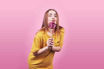 Girl cute funny portrait holding lollipop smiling on pink background. Beautiful multicultural Caucasian girl smiling happy