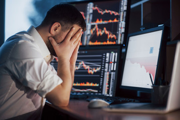 Stressful day at the office. Young businessman holding hands on his face while sitting at the desk in creative office. Stock Exchange Trading Forex Finance Graphic Concept
