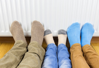 Young family warming cold feet in front of heater at home. 