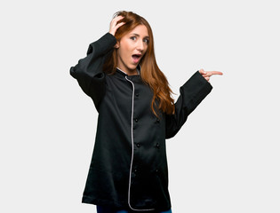 Naklejka premium Young redhead chef woman pointing finger to the side and presenting a product on isolated grey background
