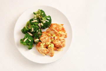 marinated chicken breast fillet with spring onions and broccoli with almond sticks, healthy meal wion a plate and on a white painted table, copy space, high angle view from above
