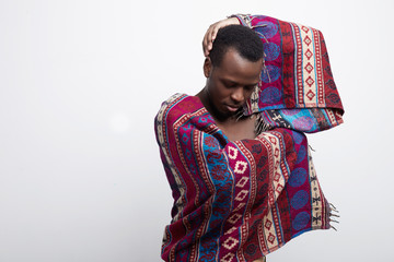 Obraz premium Authentic studio shot of graceful elegant African American man moving gently, wearing ethnic poncho, dancing to the rhythm of national music, looking down, feeling the moment, devoting himself to life