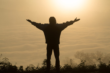 Fototapeta premium Man praying at sunset mountains raised hands Travel Lifestyle spiritual relaxation emotional concept, Freedom and travel adventure.