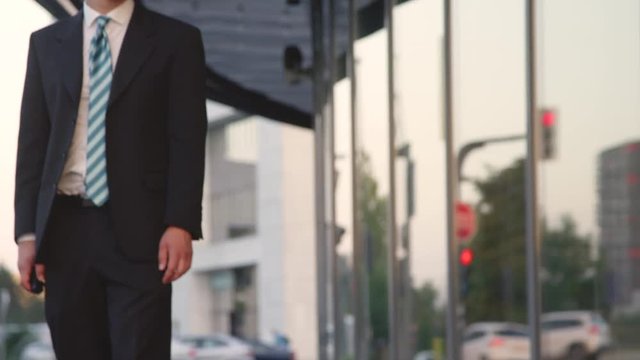 SLOW MOTION CLOSE UP: Happy businessman riding his electric skateboard through the city. Young Caucasian man in a suit longboarding to work on a sunny morning. Active manager longboarding down street.