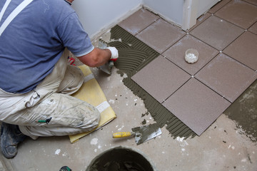 The construction worker evenly spreads the surface of the stairs with cement adhesive mass using a special hand tool.