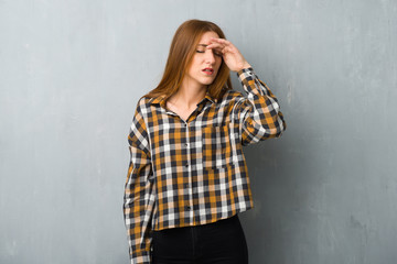 Young redhead girl over grunge wall with tired and sick expression