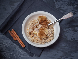 A plate of porridge with a sprinkling of cinnamon and banana circles. Shot close up on a dark wooden background.