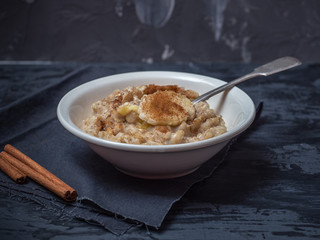 A plate of porridge, a sprinkle of cinnamon and banana circles stands on a black cotton napkin.