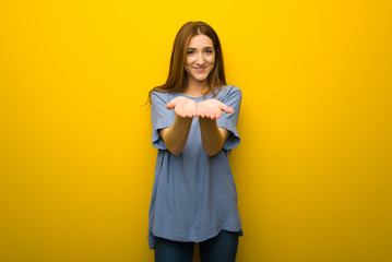 Young redhead girl over yellow wall background holding copyspace imaginary on the palm to insert an ad