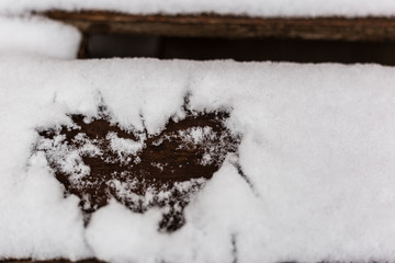 Heart drawn in the snow on a wooden bench, close up view. Valentine's day greeting card with place for text.