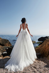 Fototapeta na wymiar Girl in wedding luxury dress posing on sea shore. Bride on a rocks.