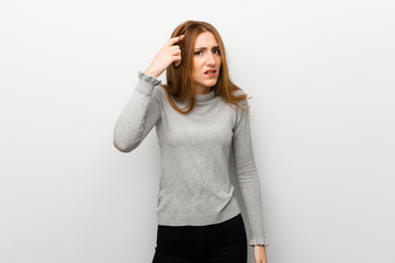 Redhead girl over white wall making the gesture of madness putting finger on the head