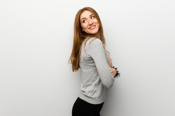 Redhead girl over white wall looking over the shoulder with a smile