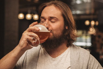 Close up of a bearded man sipping delicious craft beer with his eyes closed, resting at the bar....