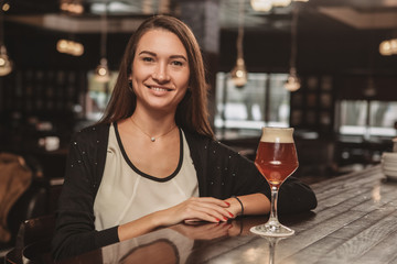 Lovely young woman smiling to the camera, resting at the local bar, having beer at the counter....