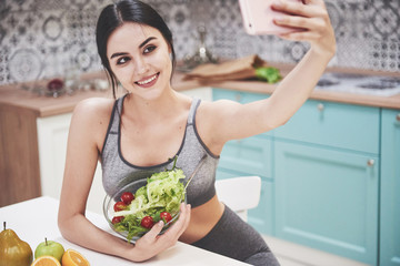 Young woman eating healthy salad with cherry tomatoes in the kitchen after a fitness session