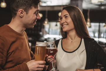 Beautiful happy couple looking at each other with love, celebrating their anniversary, having drinks at the restaurant together. Beautiful woman and her handsome boyfriend drinking craft beer