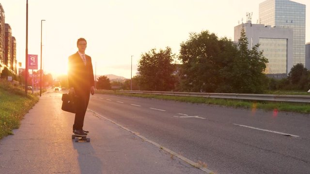 SLOW MOTION, LENS FLARE: Cool sporty businessman going home from work on his e-skateboard. Cheerful yuppie cruising through the city on a sunny summer evening. Happy young man enjoying his ride home.