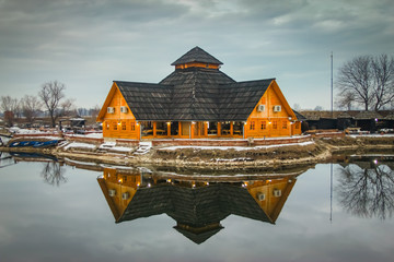 Naklejka na ściany i meble Wooden restaurant near the frozen pond in sunset, winter cloudy day